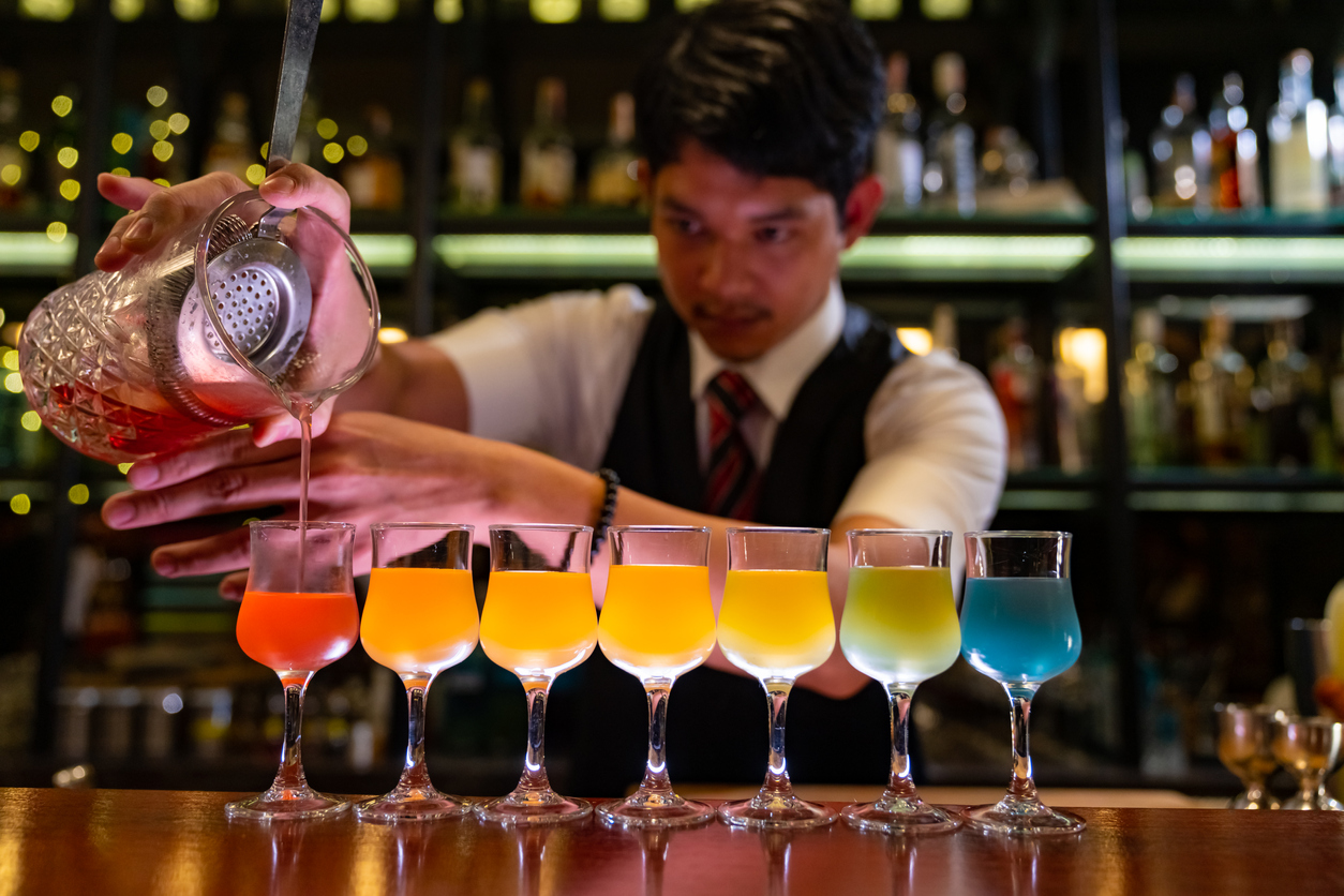 Professional male bartender preparing colorful cocktail drink serving to customer on bar counter at nightclub. Barman making mixed alcoholic drink for celebrating holiday event party at luxury restaurant bar.